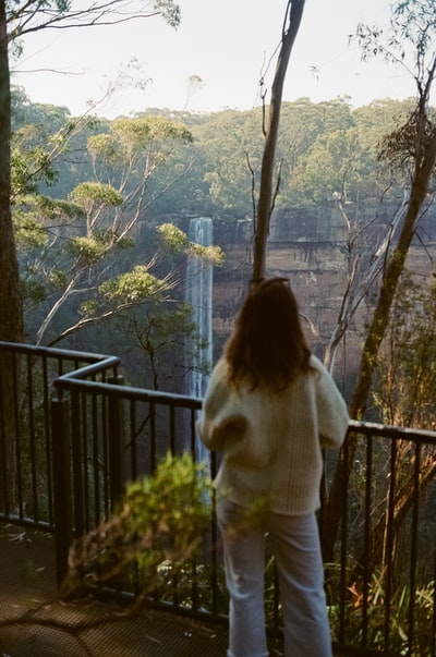 The woman stood on the balcony during the day wearing a white sweater
